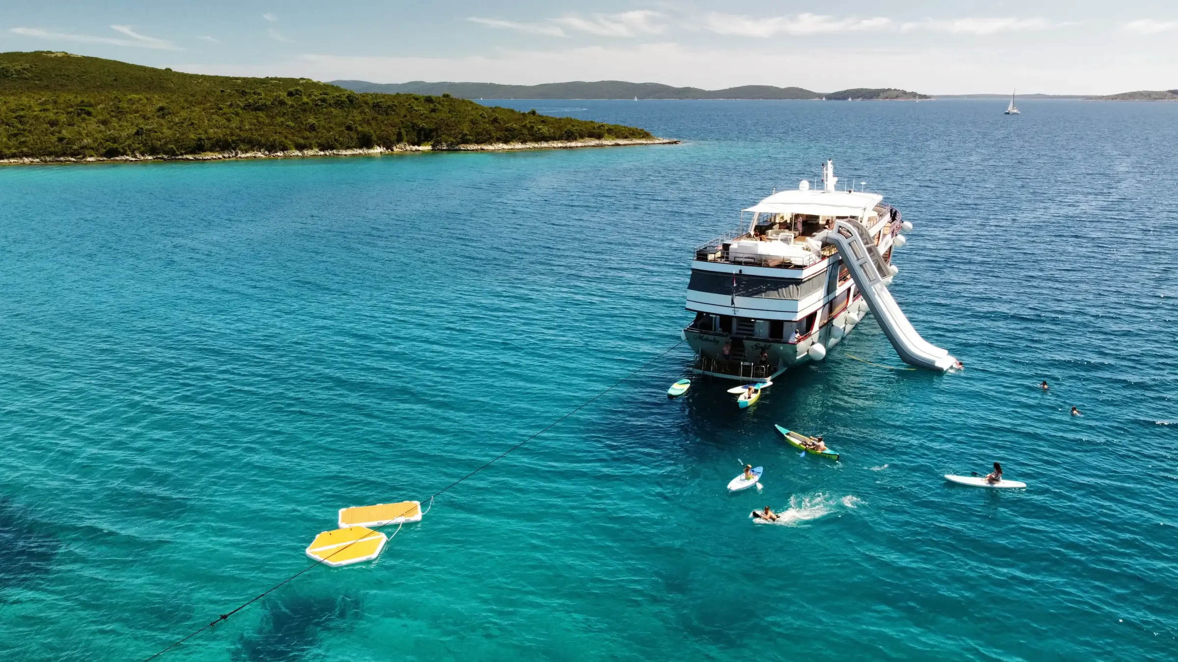 MS Melody anchored in a turquoise bay with paddle boards and a floating platform